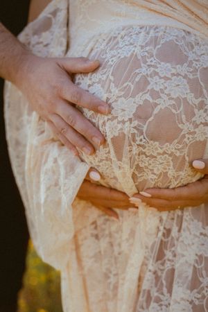 Close-up of hands cradling belly through delicate lace maternity dress.