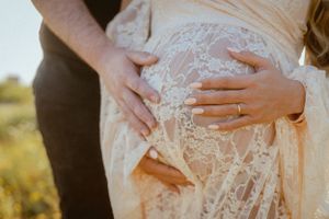 Gentle hands rest on pregnant belly covered in flowing lace dress.