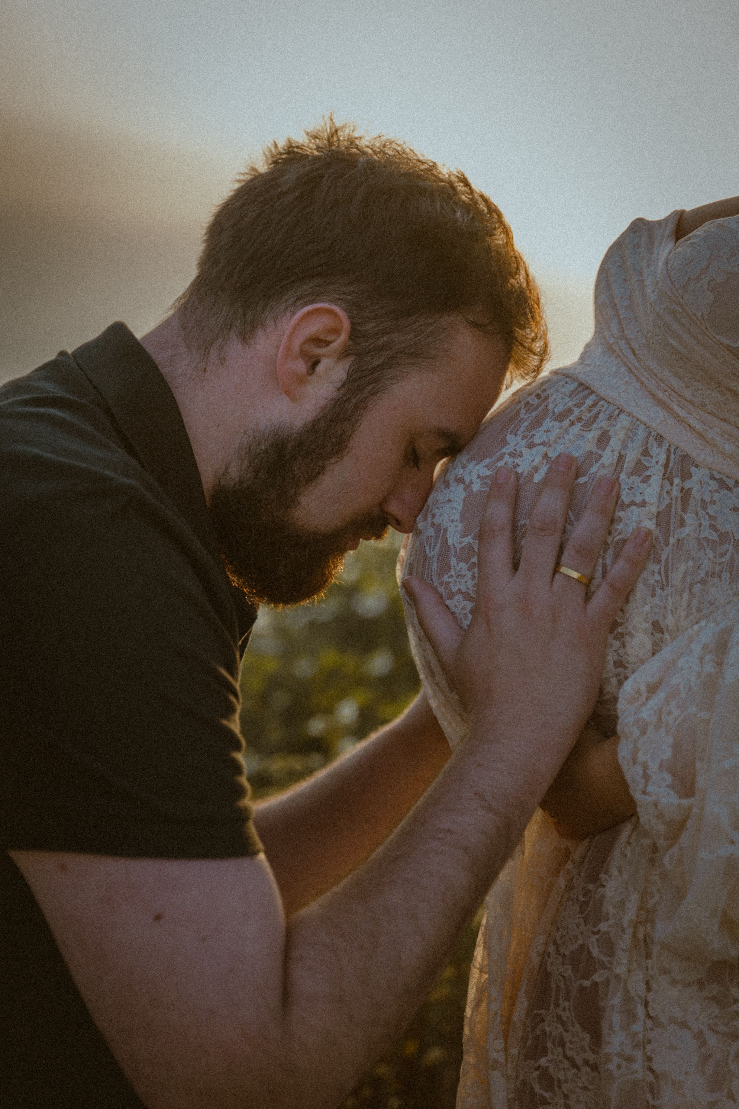 An intimate maternity moment captured with man embracing baby bump through lace dress.