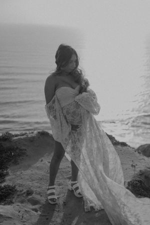 Black and white photograph of couple on rocky beach with delicate lace dress.