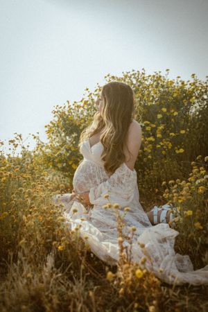 Person in white lace dress sitting among yellow wildflowers during golden hour.