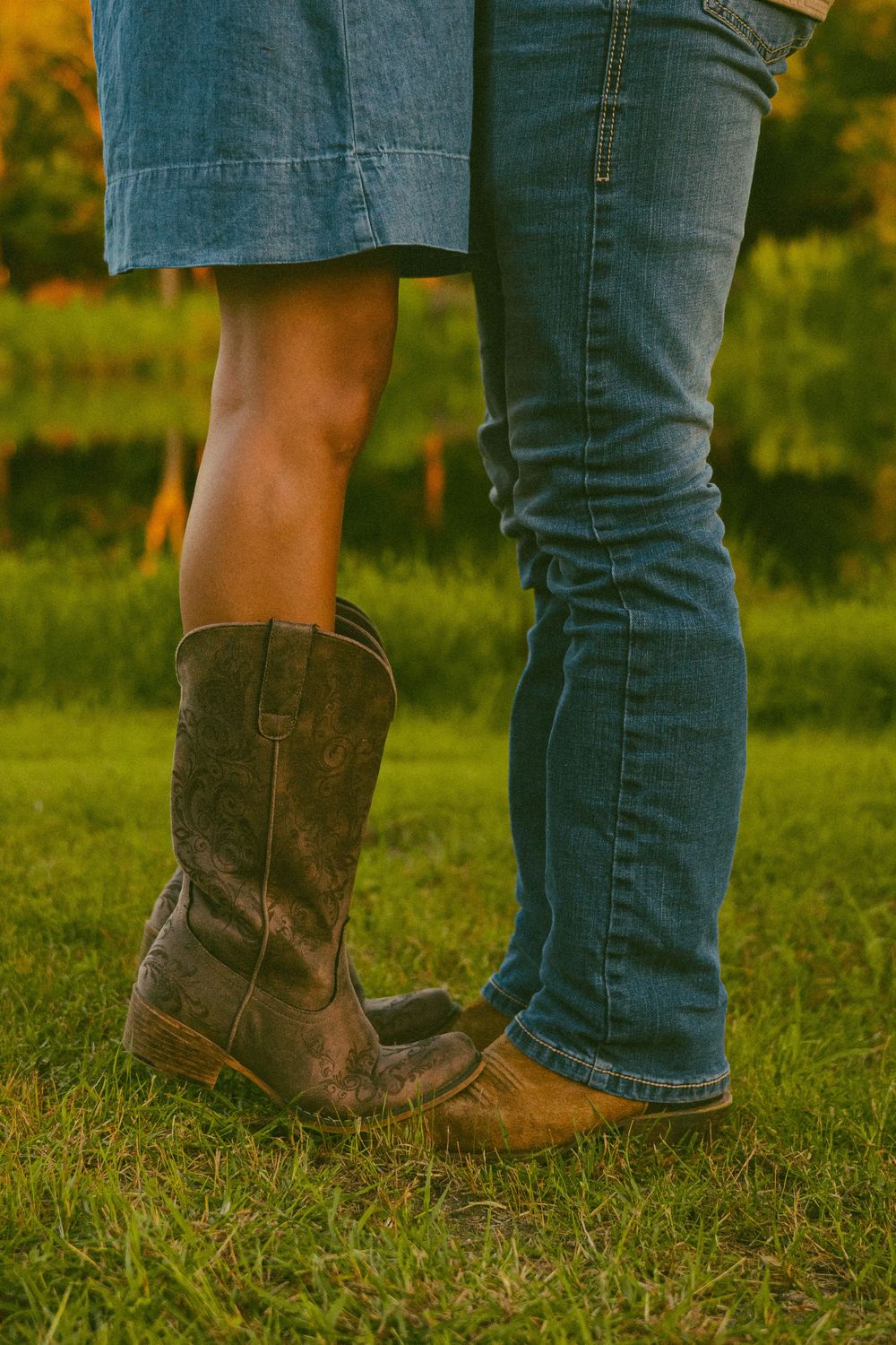 Close-up of couple standing on grass, woman in denim skirt and cowboy boots, man in blue jeans and brown boots.