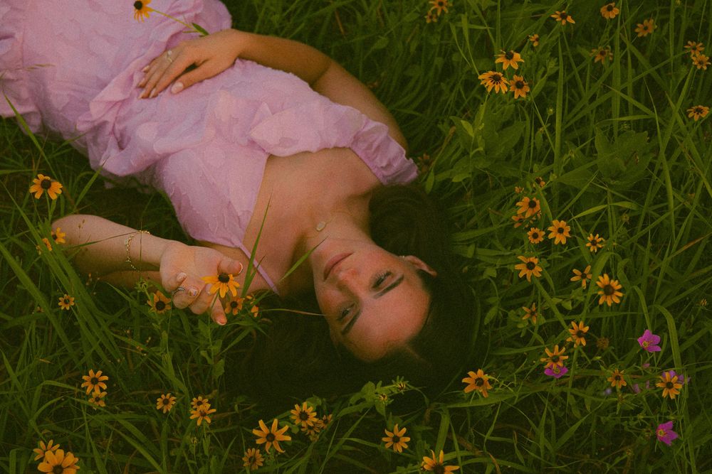 A young woman in a pink dress lying peacefully in a lush green meadow surrounded by colorful wildflowers.