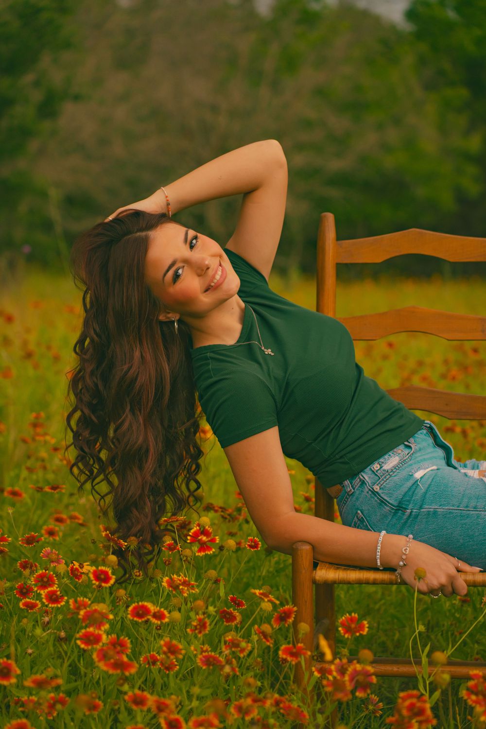 Woman in green top reclines on wooden chair among blooming wildflowers at sunset.