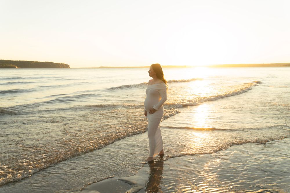 Silhouette of a pregnant woman standing in shallow ocean waves during golden sunset.