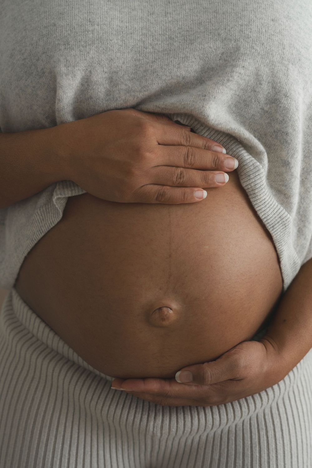 Close-up of hands gently cradling a pregnant belly wearing a grey sweater.