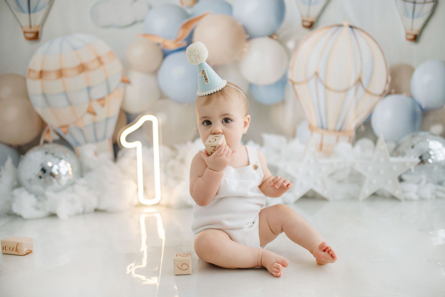 A baby's first birthday setup with pink balloons, glitter trees and a matching cake.