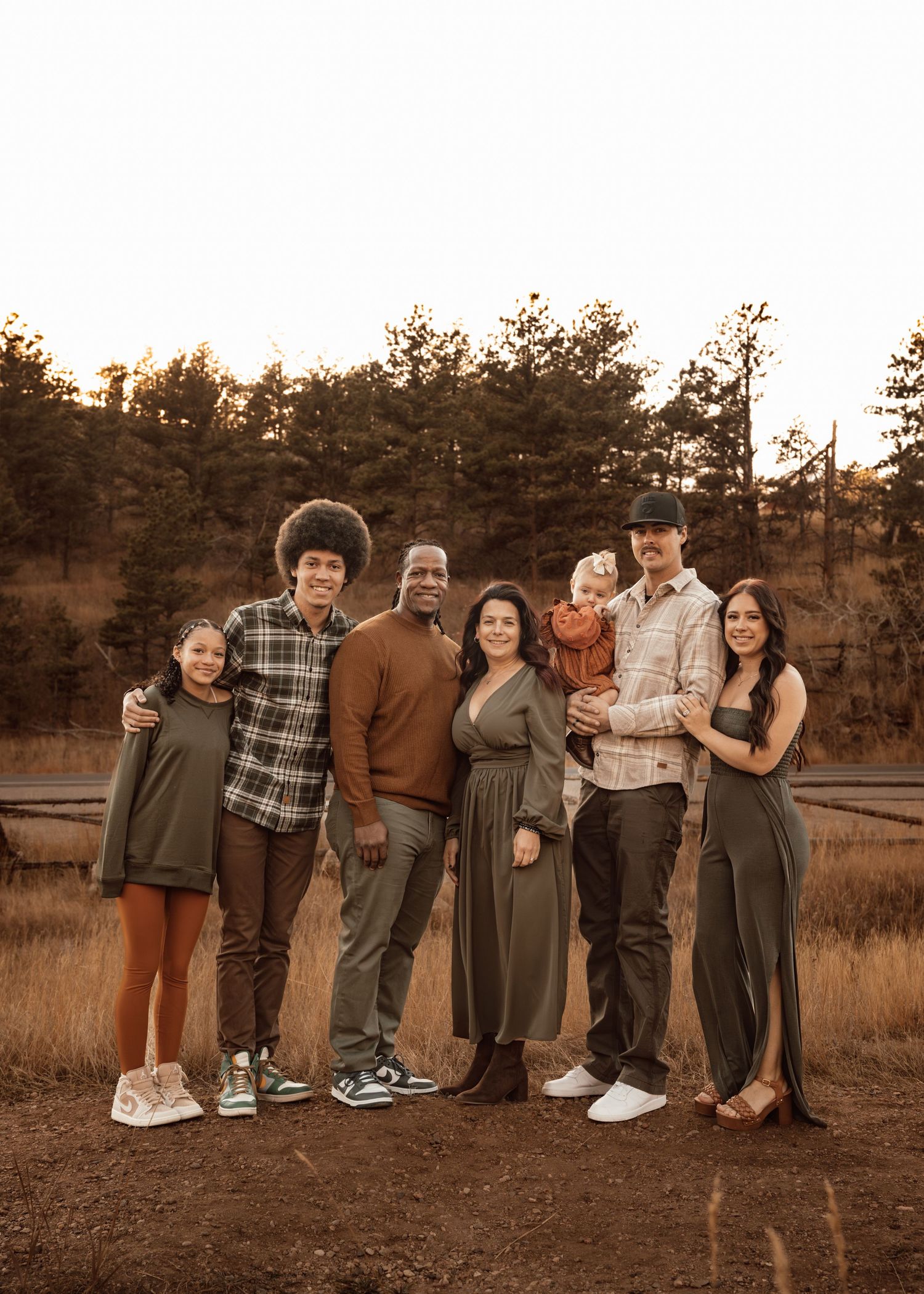 A family photo session outdoors on a grassy hillside with rustic western attire.