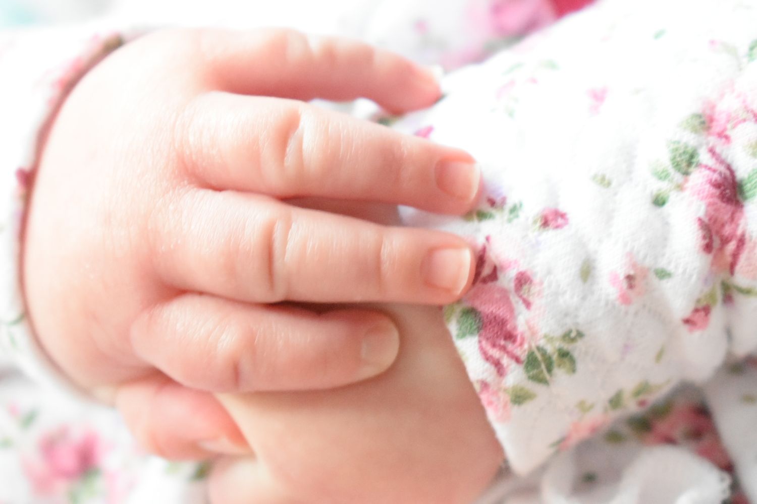 Close-up of tiny baby hands against floral patterned fabric.