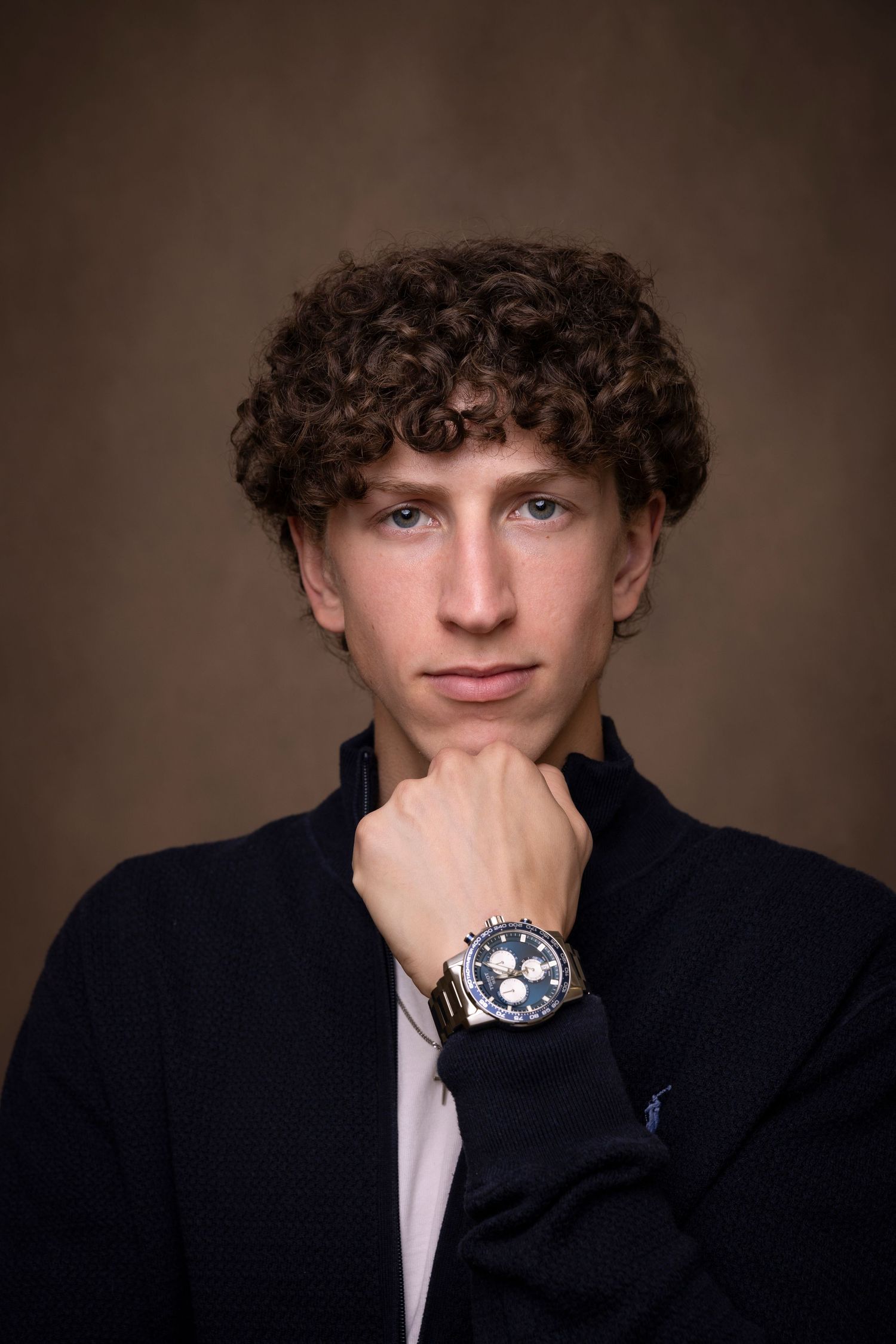 Stylish portrait of young man in dark blazer against brown backdrop.