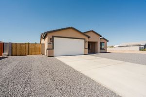 Single story house with beige exterior and white garage door features gravel driveway and wooden fence under blue sky.