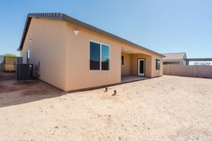 Beige stucco house with covered patio and backyard dirt lot in desert landscape setting.
