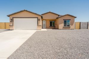 Single-story beige stucco house with two-car garage and gravel landscaping in desert setting.