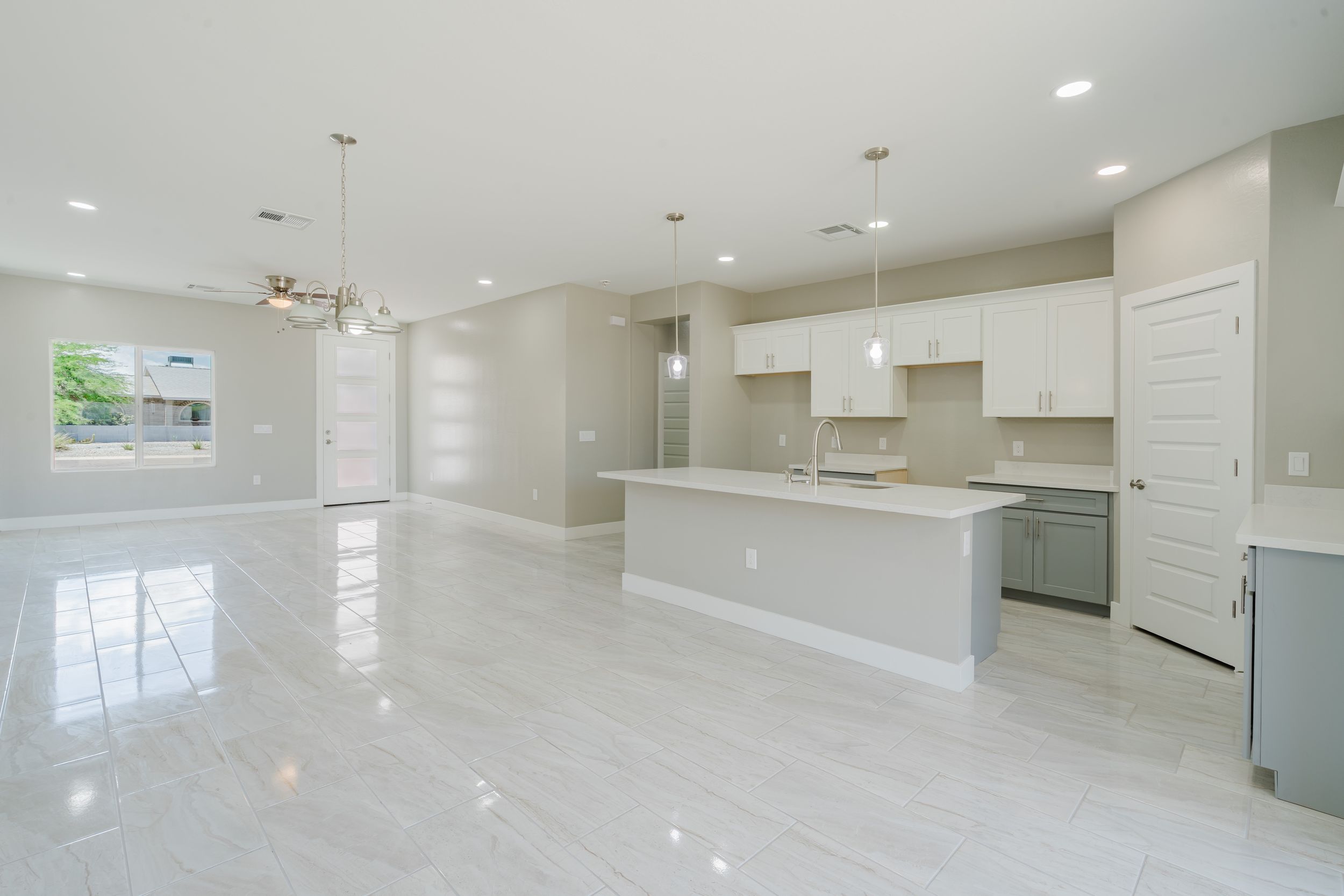 Modern open concept kitchen and living room with white cabinets, grey floors, and pendant lighting in a minimalist design.