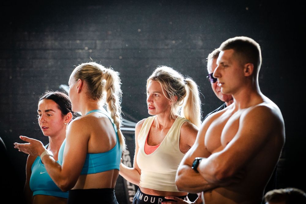 Athletes in workout gear perform intense exercises in a dimly lit gym setting.