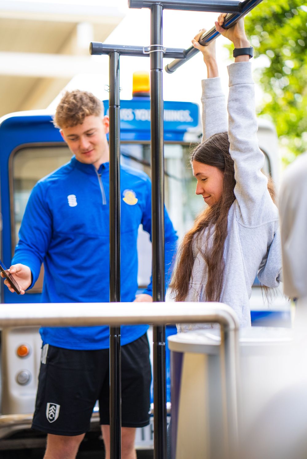Students in school uniforms interact with a metal pole structure in an outdoor setting.