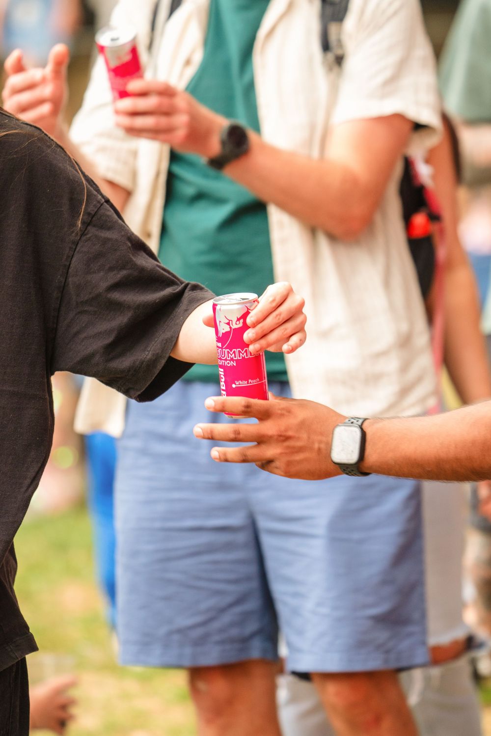 Hands passing pink beverage cans in a crowd during an outdoor event.