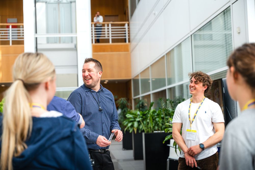A small group of people having an animated conversation in a modern office lobby with glass walls and plants.