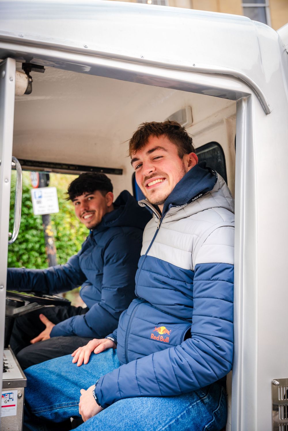 Young people in blue winter jackets sitting and smiling together inside a vehicle.