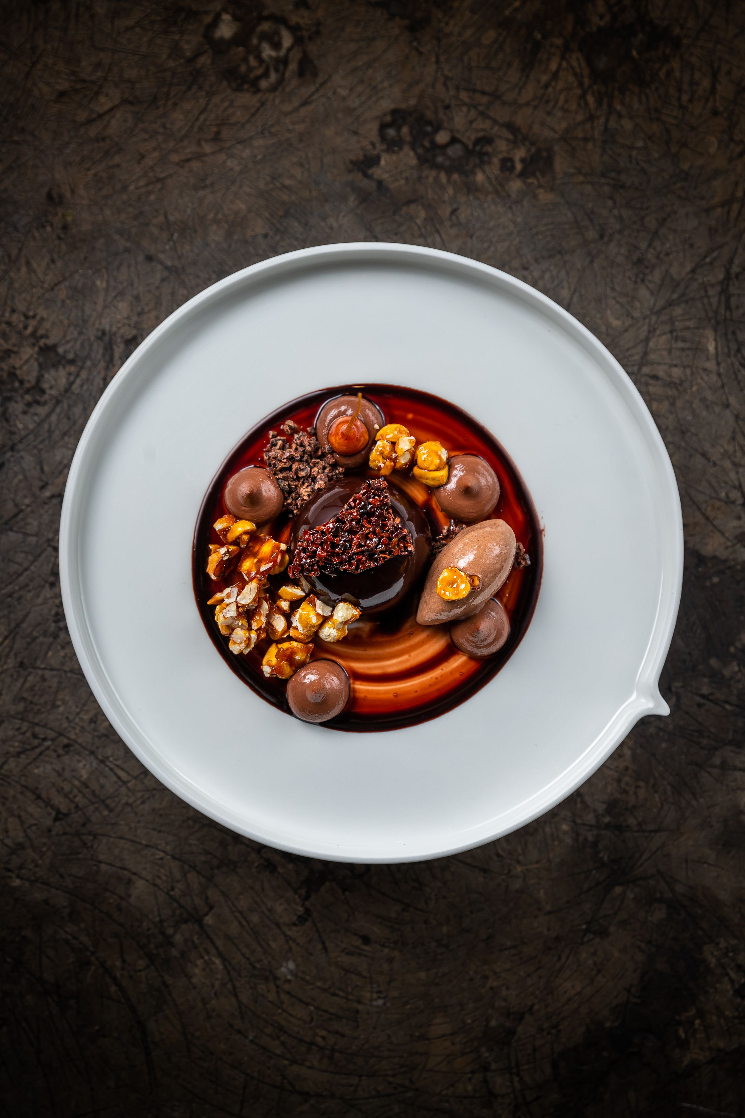 Gourmet plated dessert with chocolate and caramel elements on white ceramic dish.