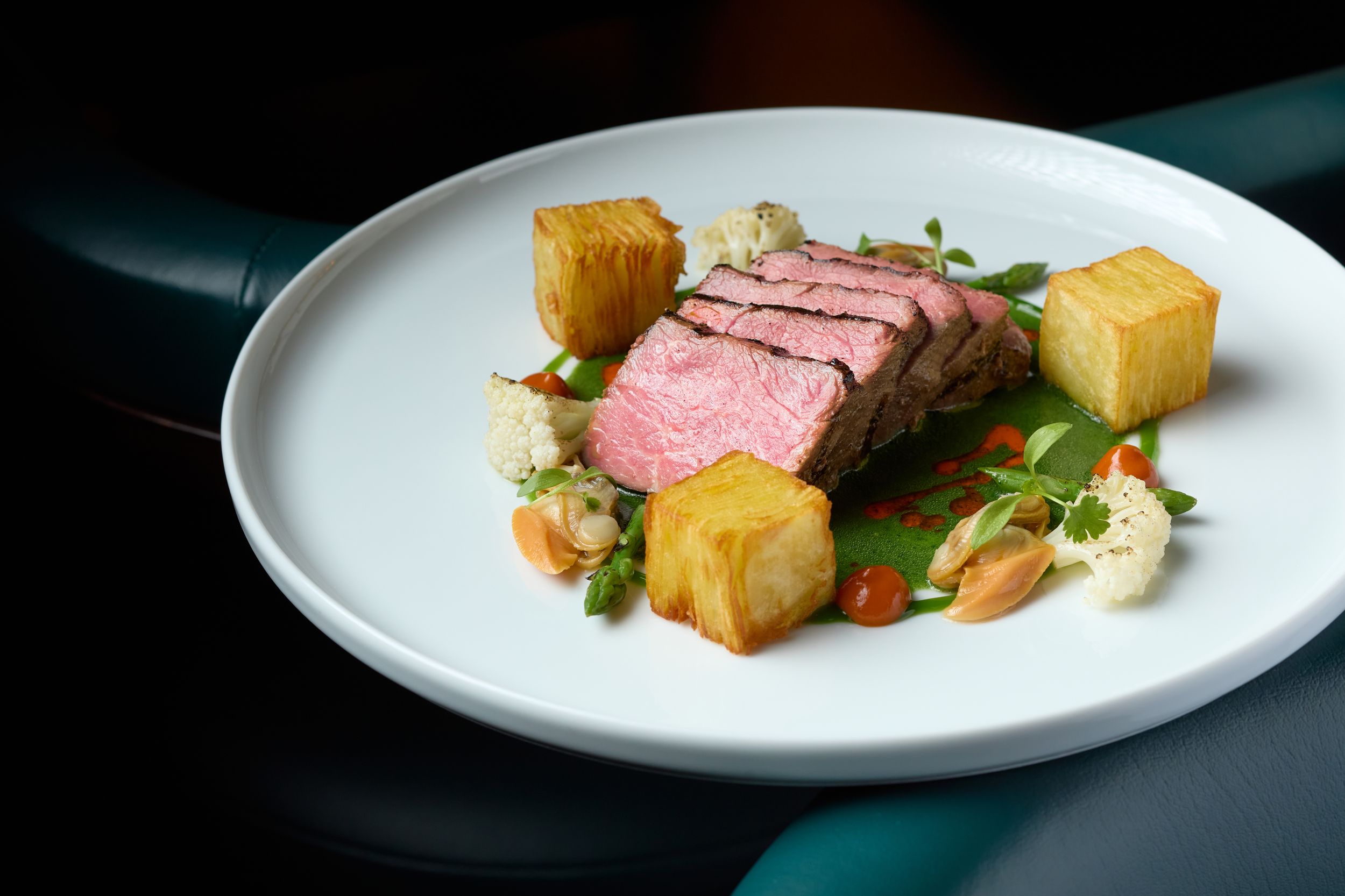 Medium-rare sliced steak plated with golden cubes and microgreens on white ceramic dish.