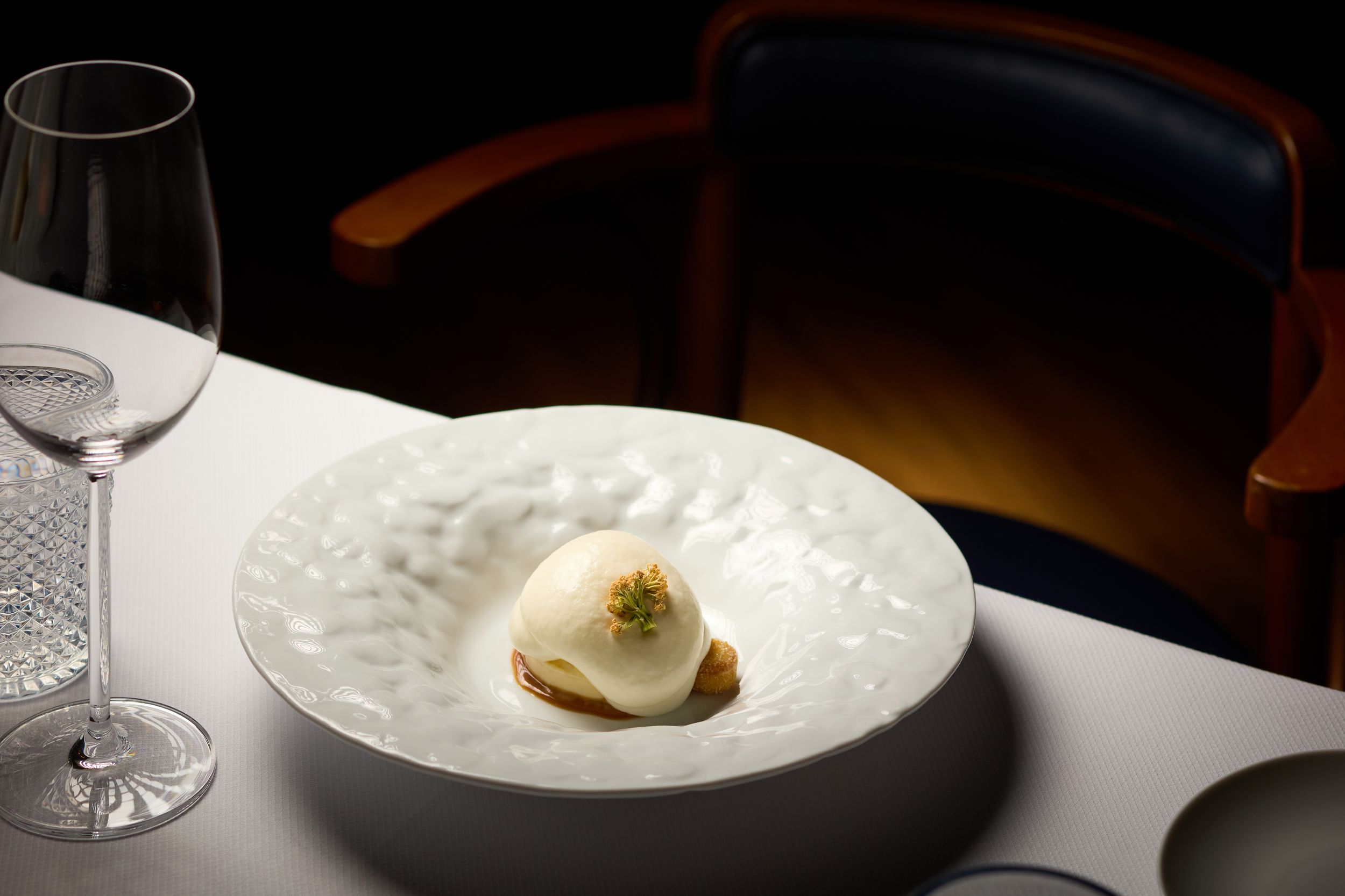 Elegant plated dessert on white textured china with wine glass in dramatic lighting.