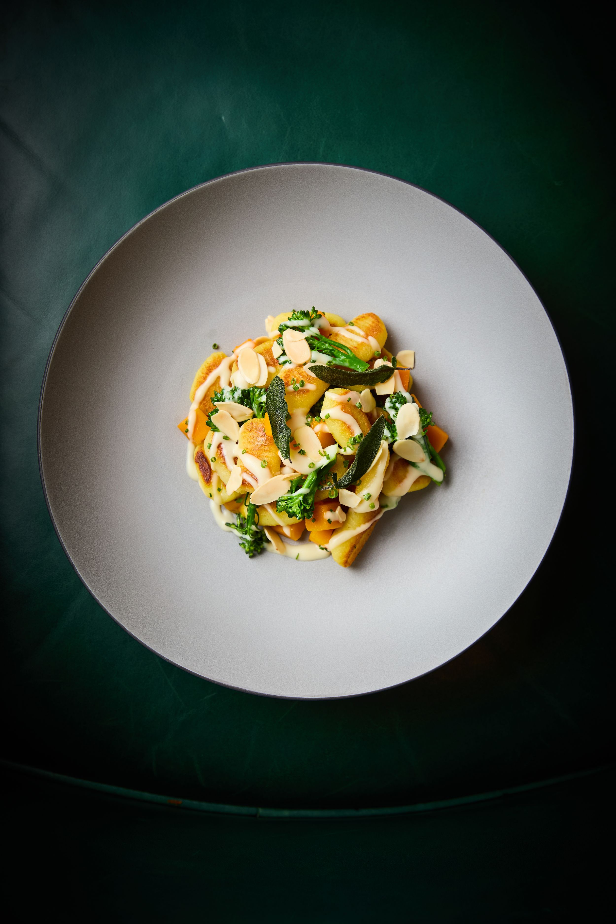Fresh pasta dish with herbs and vegetables plated on white ceramic plate against dark background.