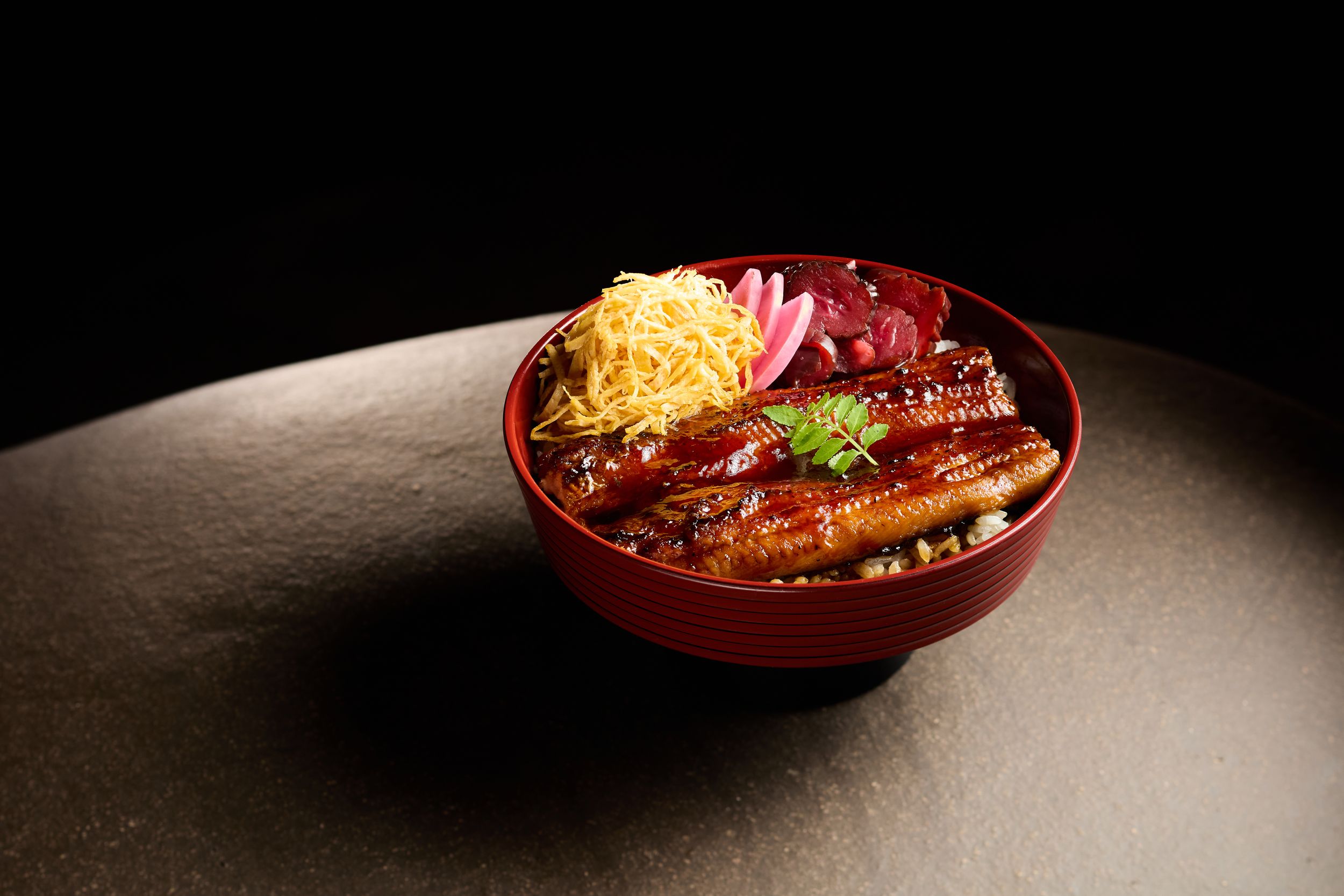 Japanese rice bowl with grilled meat, shredded vegetables and garnishes in dark lighting.