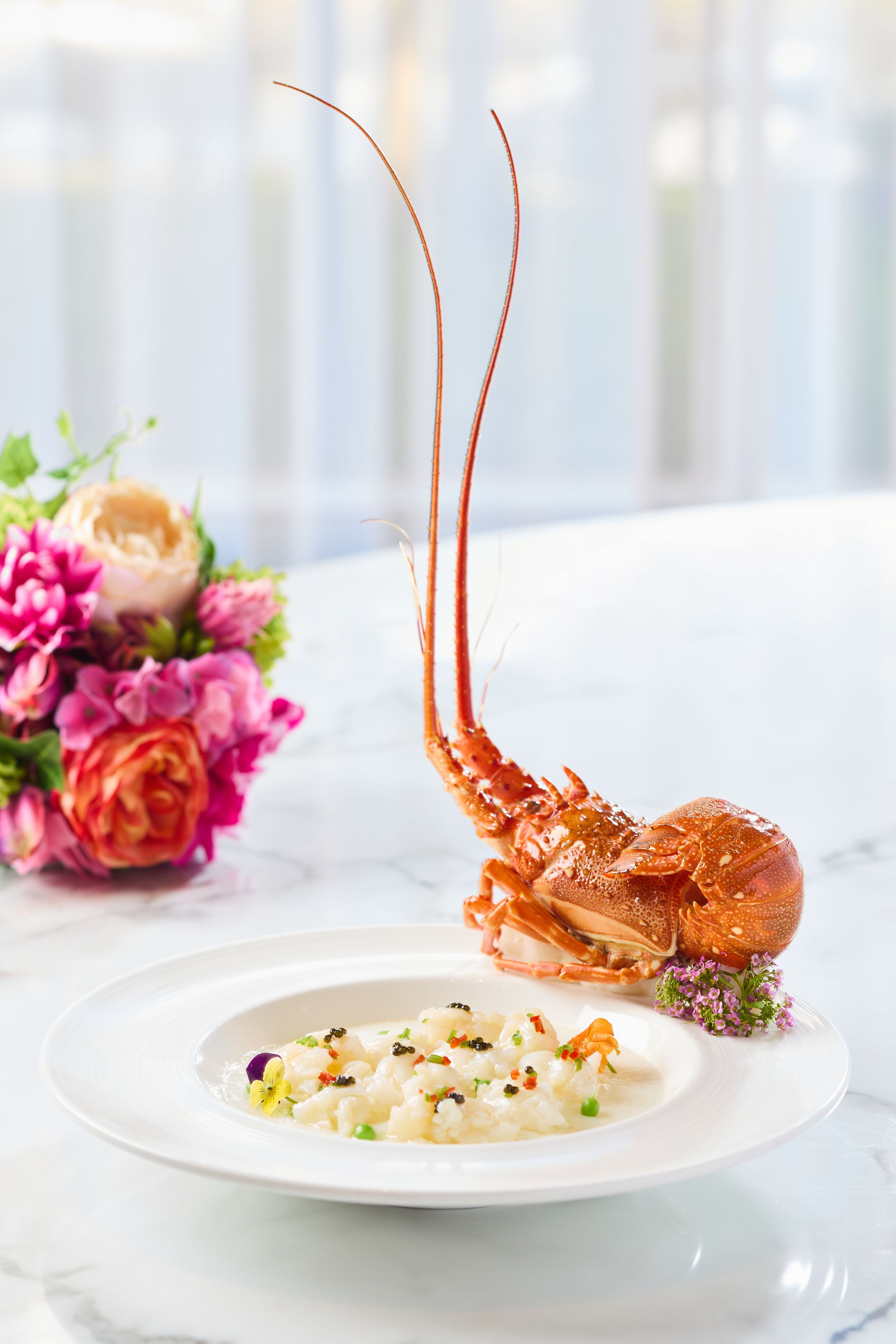 Elegant lobster dish with long antennae presented on white plate with floral decoration.