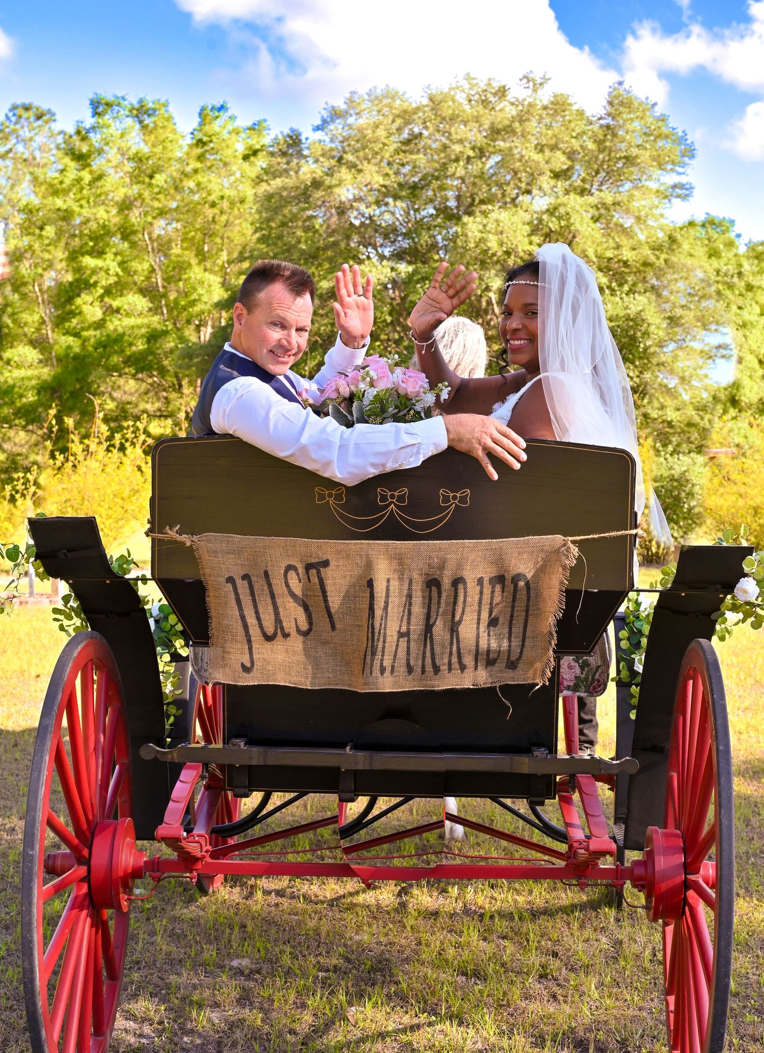 Newlyweds celebrating behind rustic wooden 'Just Married' sign outdoors.