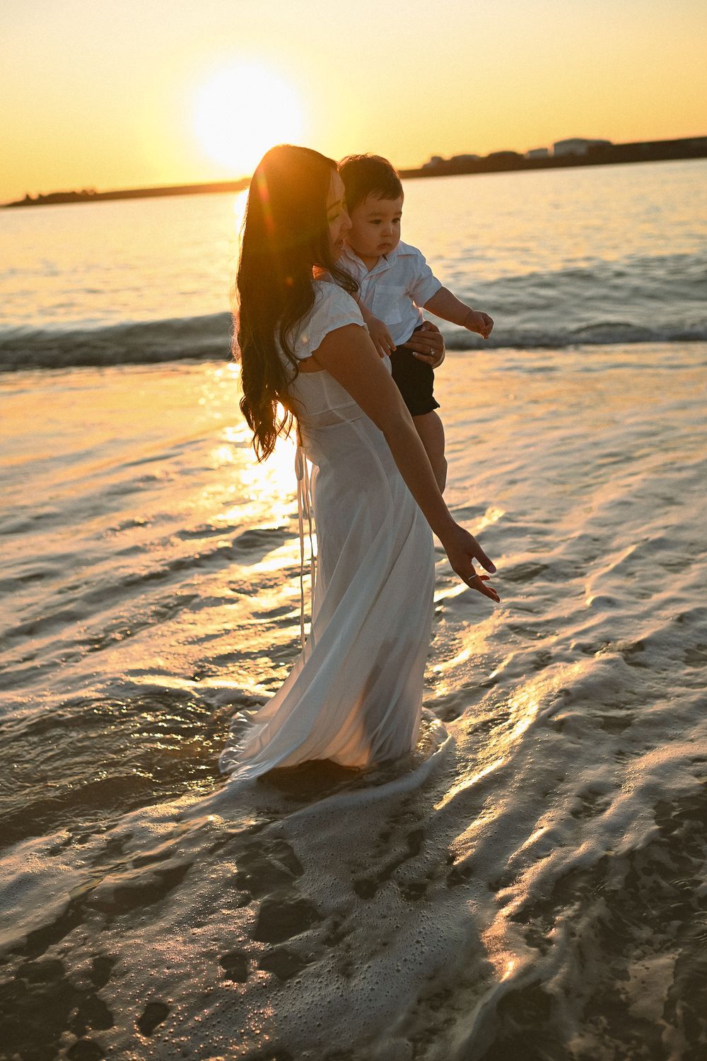 Couple splashing in ocean waves during golden hour at the beach.