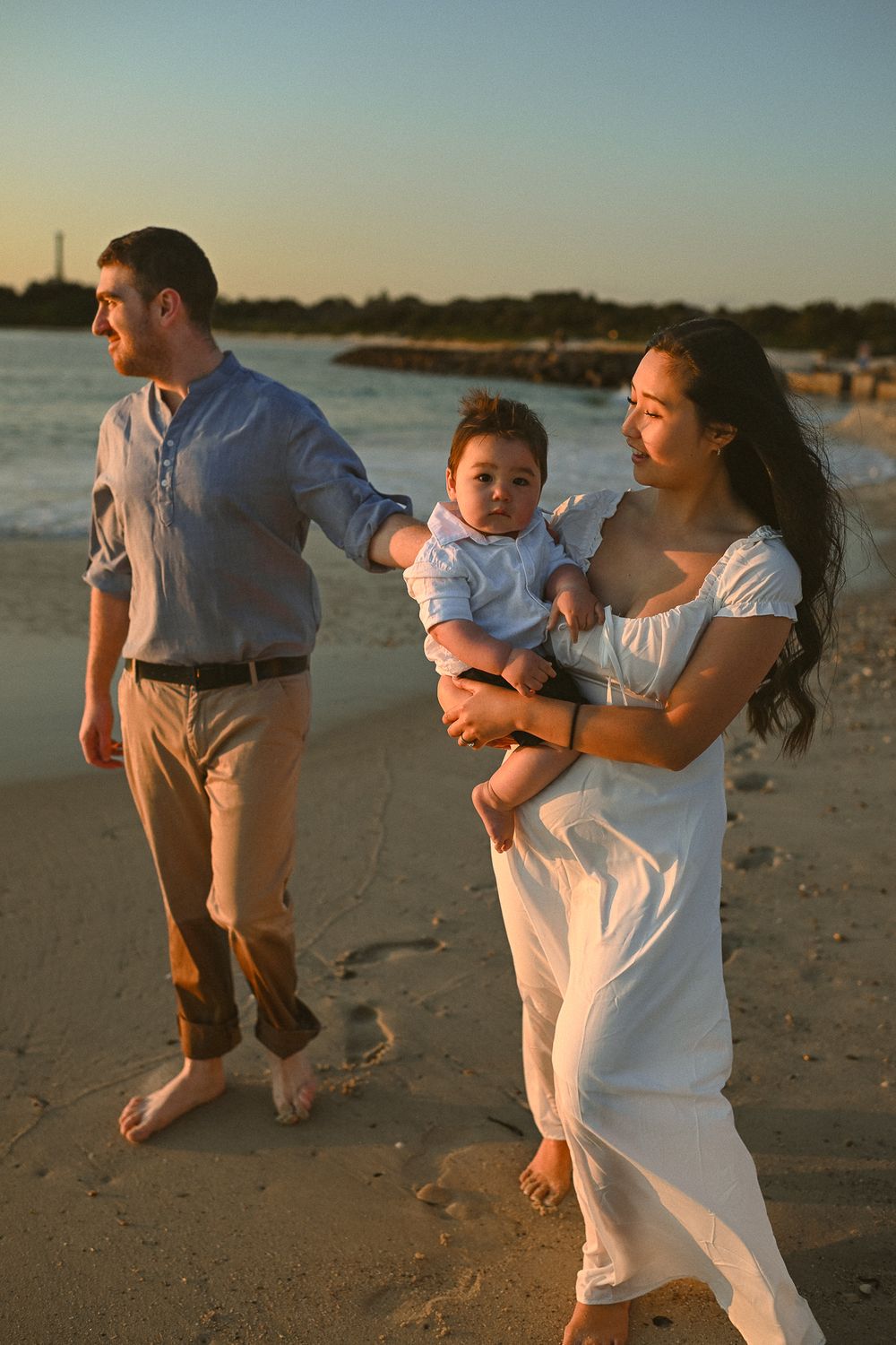 Family plays together on sandy beach at dusk, running and swinging child in joyful moments by the ocean.