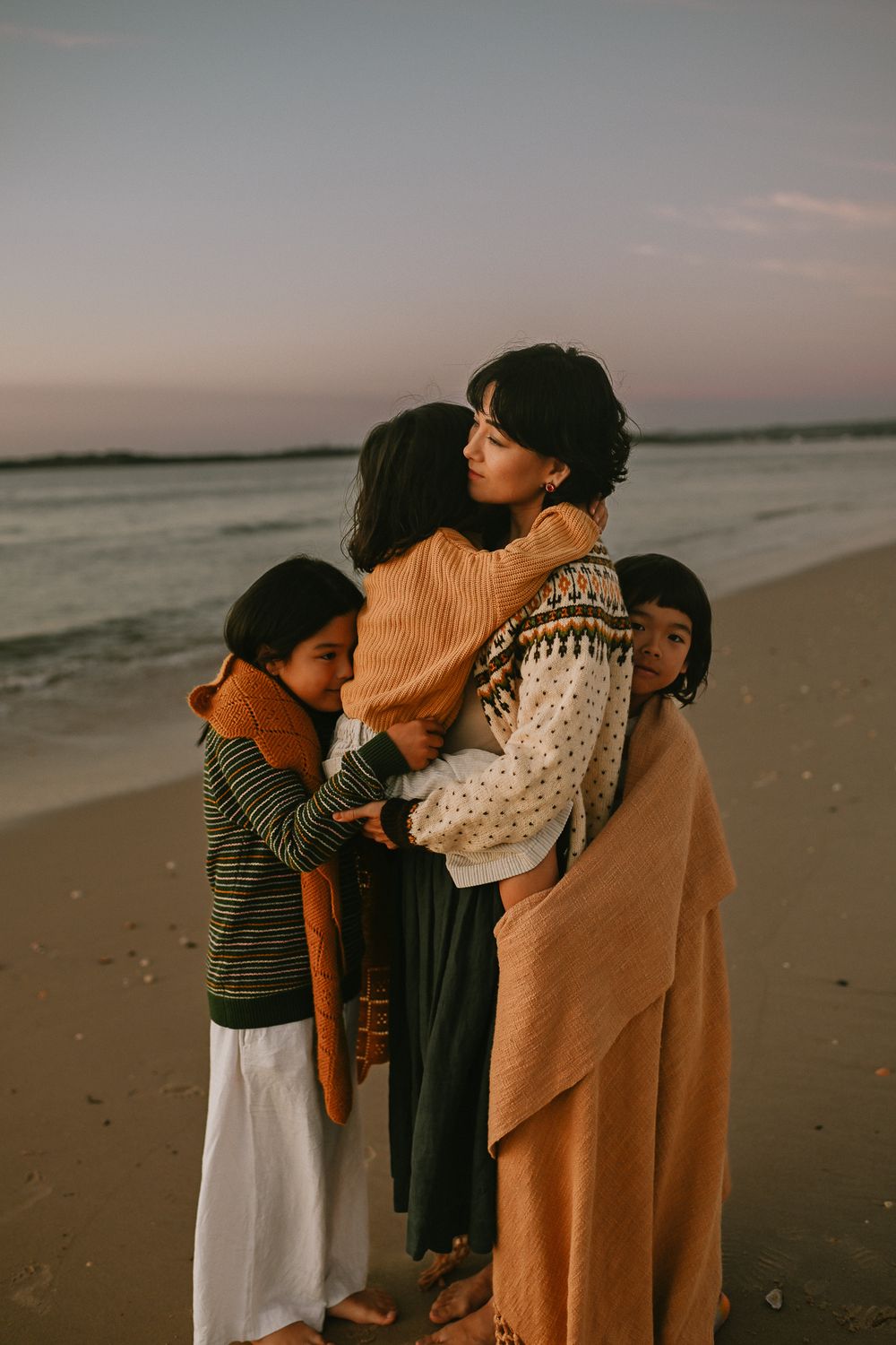 A family shares tender embraces while standing together on a serene beach at sunset.
