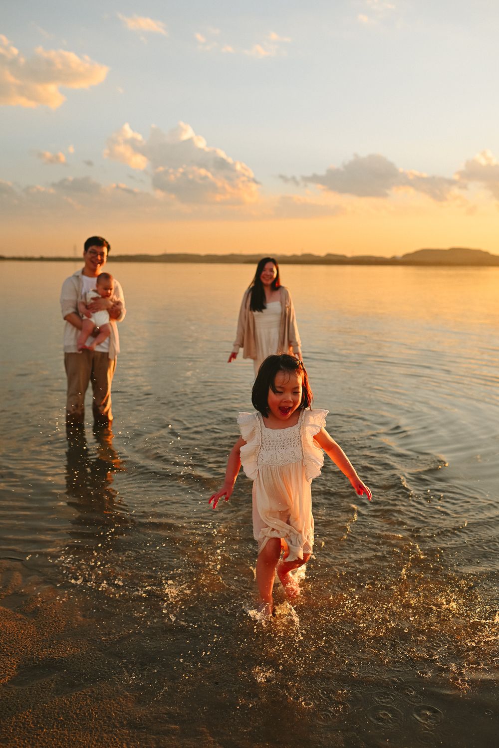 Couple playing and splashing in shallow ocean water during golden sunset hour.