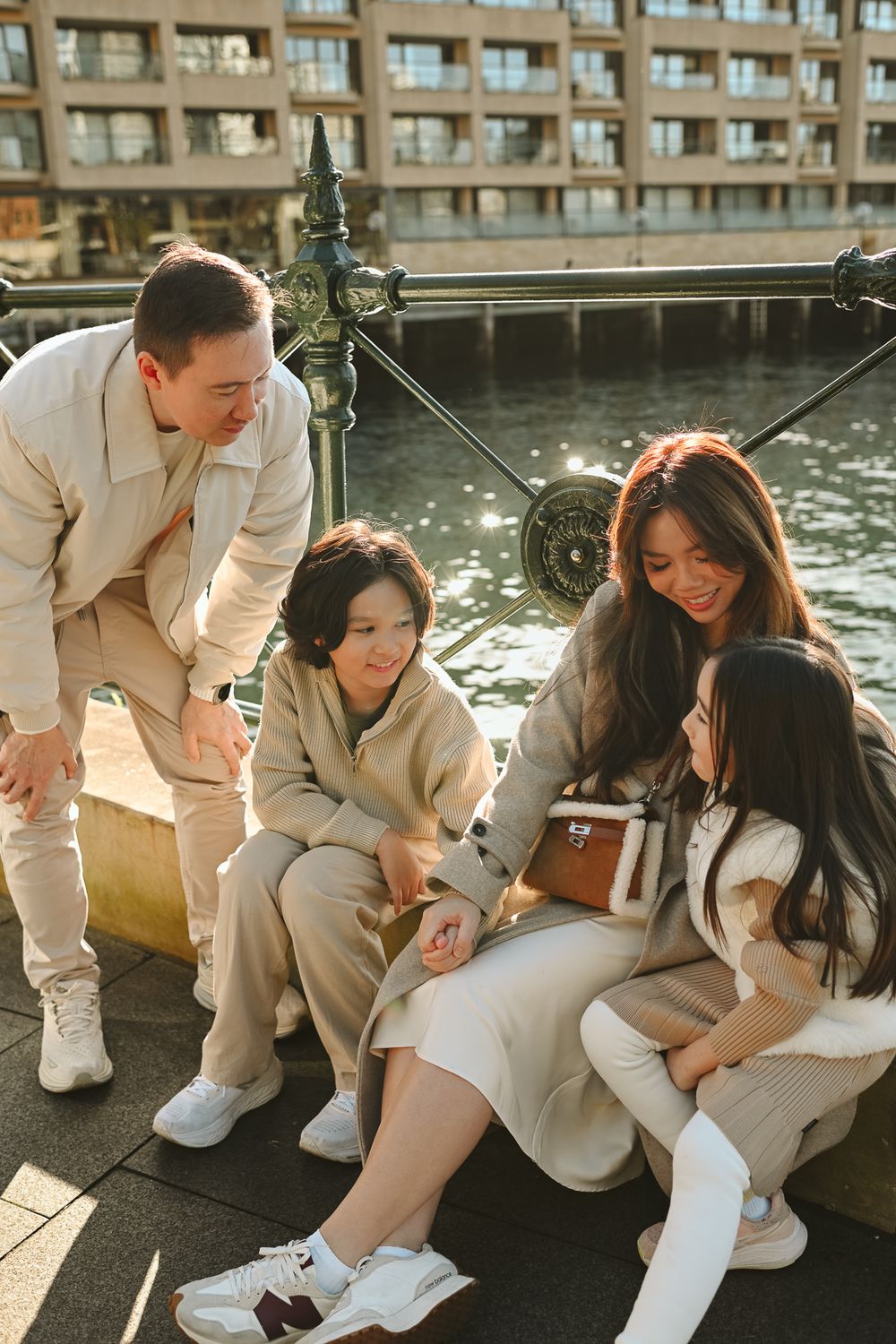 Group of friends sitting together by a waterfront on a sunny day sharing casual moments in neutral-toned outfits.