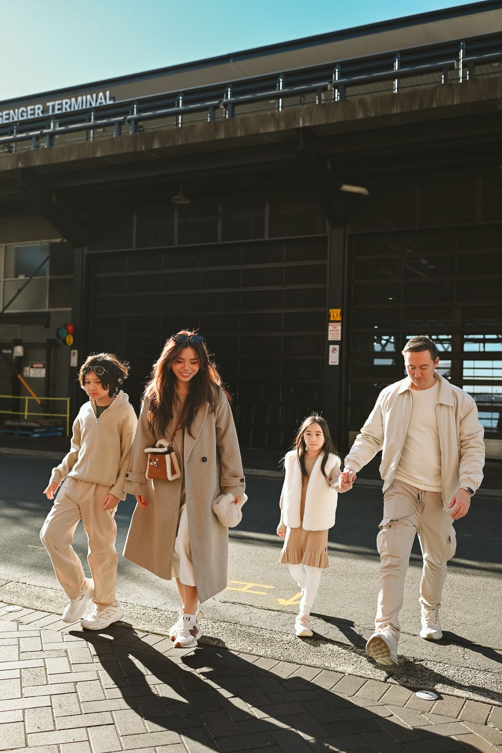 Group wearing coordinated cream colored outfits walking in line casting shadows on concrete pavement.