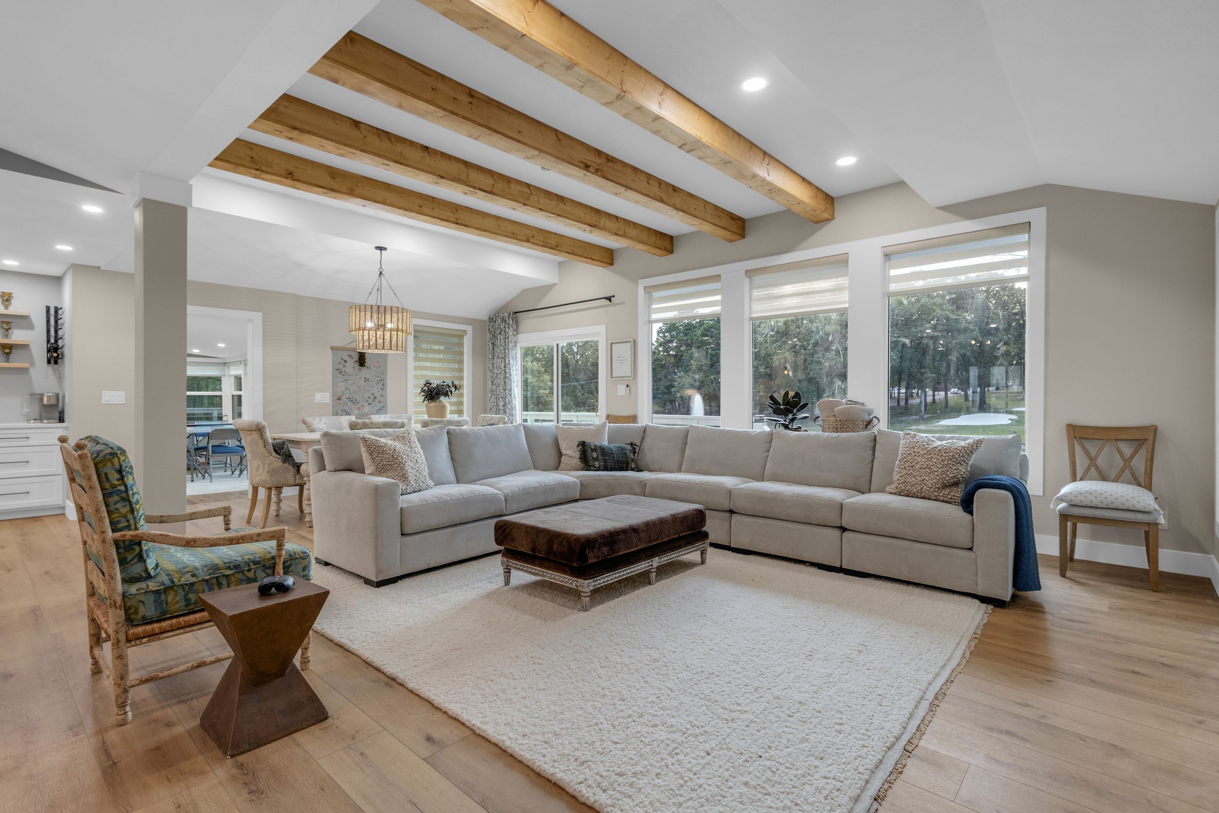 Modern living room with wood beam ceiling accents features grey sectional sofa and expansive windows for natural light.