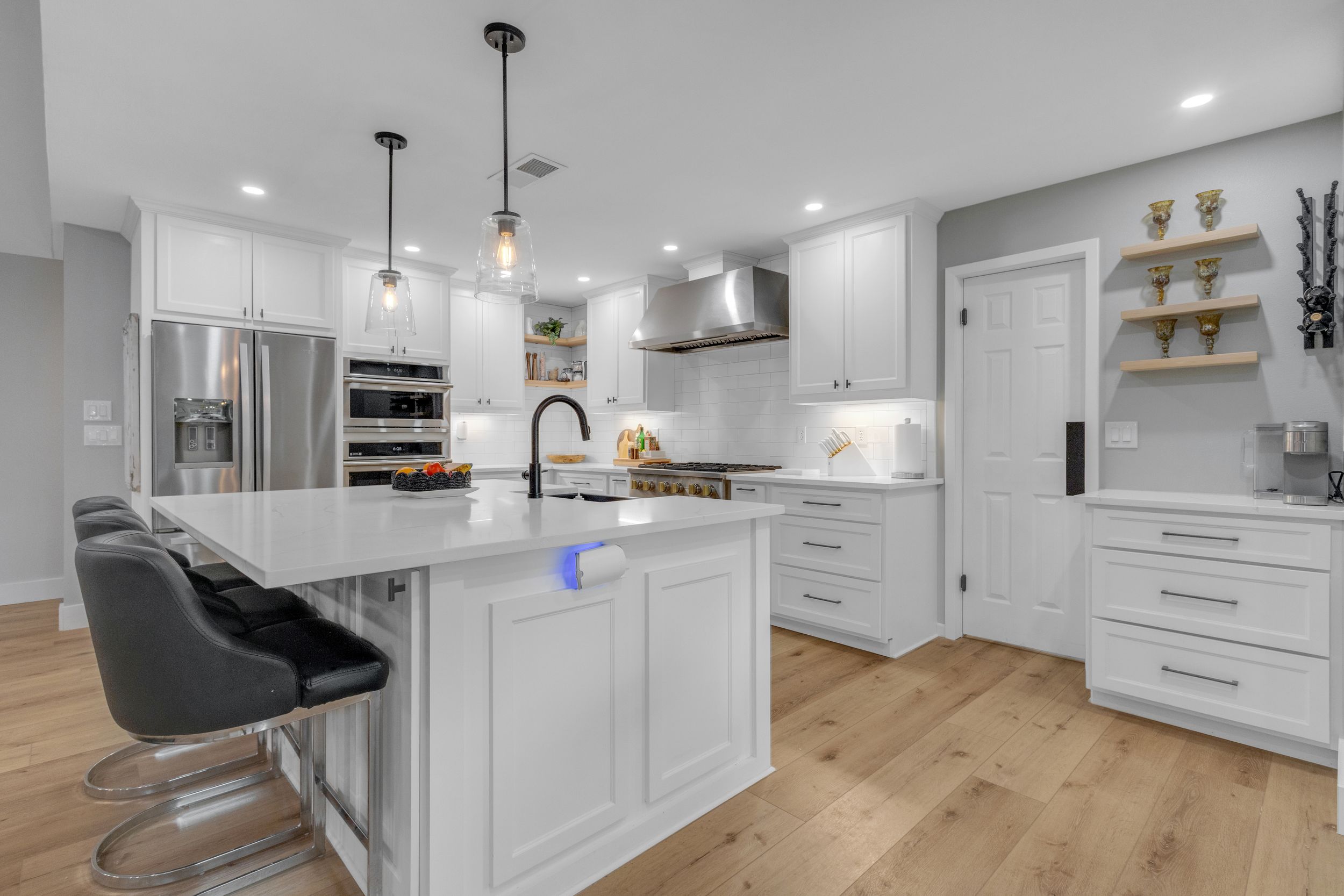Modern white kitchen with quartz island, pendant lights, stainless appliances and light hardwood floors.