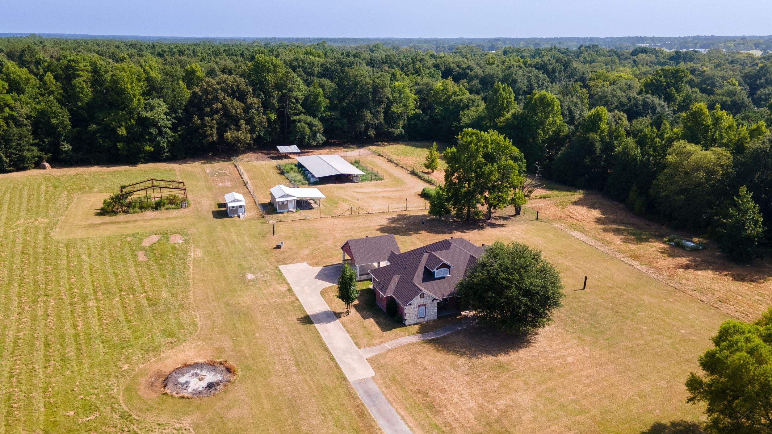 Aerial view of a rural property featuring a brick home, outbuildings, and vast green fields surrounded by dense woodland.
