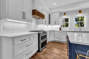 Contemporary white kitchen with navy island, quartz countertops, and stainless steel appliances.