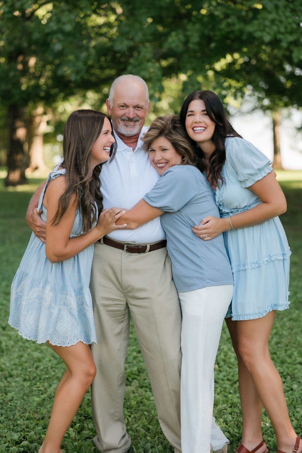 A family sharing a joyful embrace outdoors in coordinated light blue and white outfits on a sunny day.