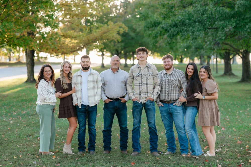 A group of people in casual clothing stands together outdoors in a park setting during golden hour.
