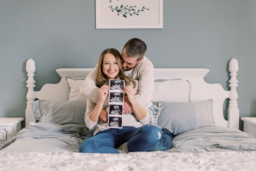 Heartfelt pregnancy announcement of a couple nestled on bed, holding sonogram, in Columbia, MO.