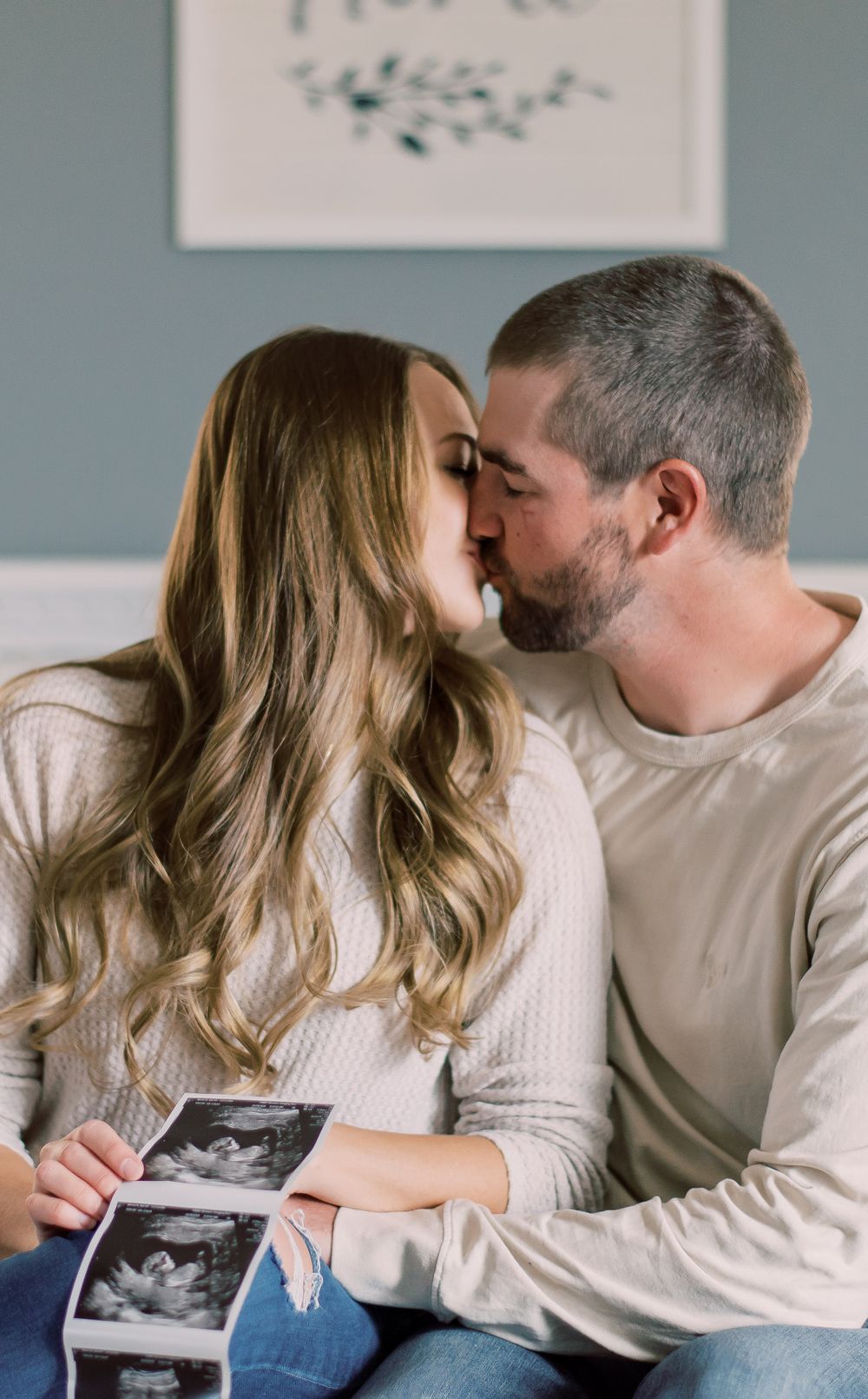 Sweet moment of a couple sharing their pregnancy news, holding sonogram, nose to nose in Columbia, MO living room.