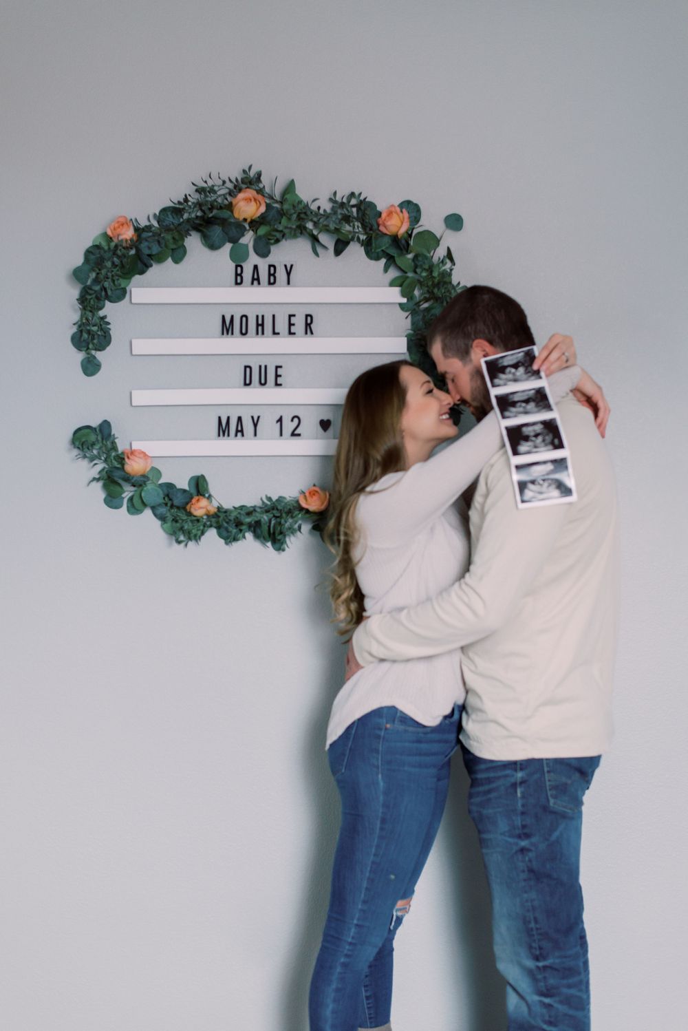 Pregnancy announcement photo of a couple surrounded by roses in the comfort of their Columbia, MO home, sharing a joyful moment.