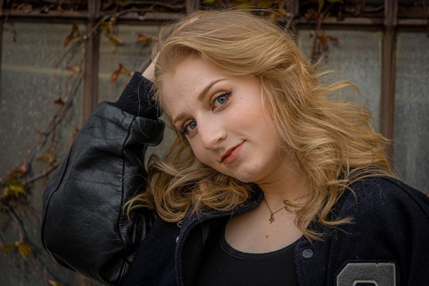 Young Woman wearing letter jacket posing in front of fence