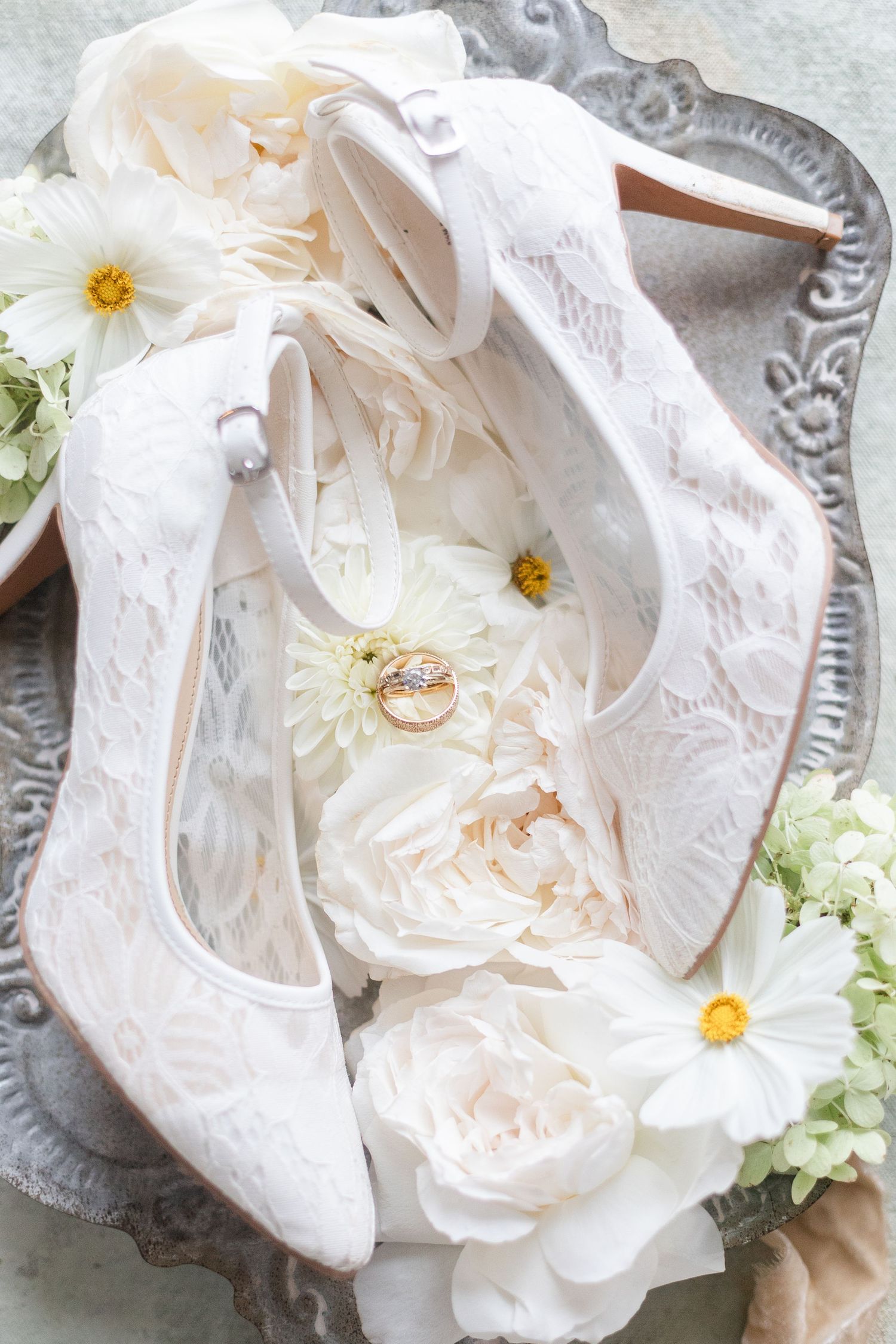 Wedding details featuring white lace shoes and delicate floral arrangements on silver trays.