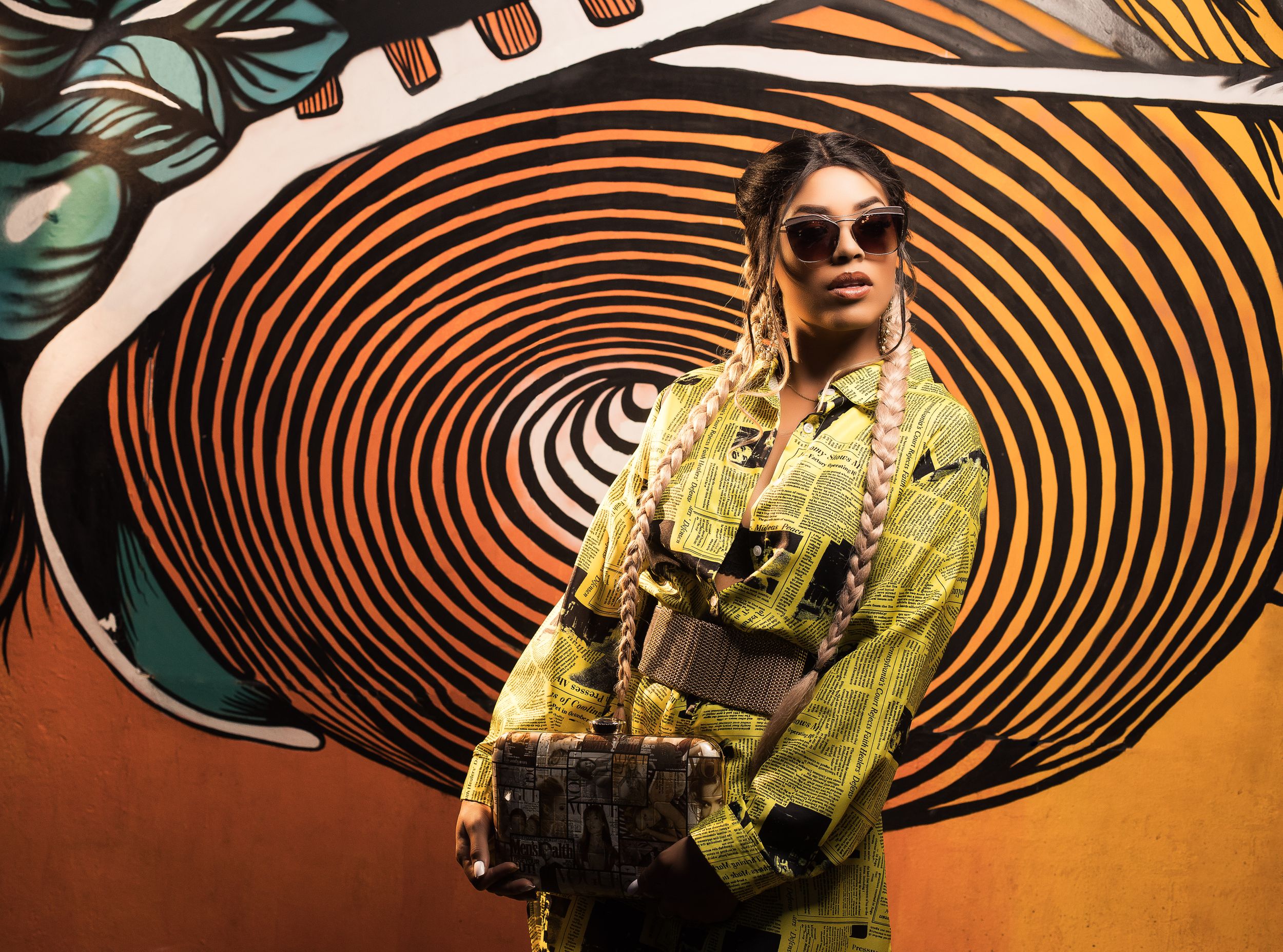 Fashion shot against spiral art mural wearing yellow outfit and sunglasses.