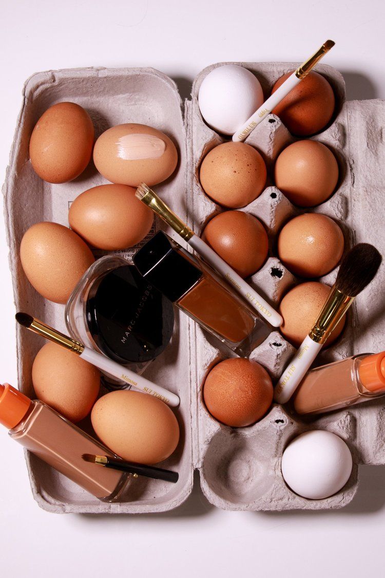 Brown and white eggs in carton with makeup brushes and cosmetics.
