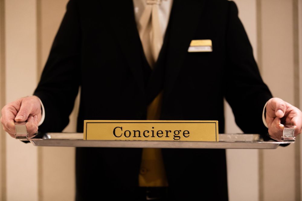Close-up of hotel concierge desk nameplate with suited staff member.